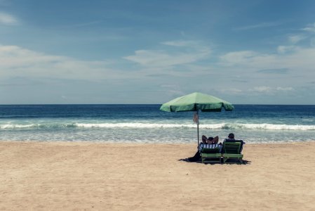 people sitting on seashore under green umbrella during daytime photo