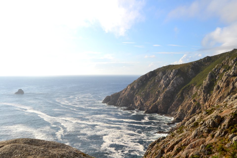 sea hitting seashore beside brown rock mountains under blue sky