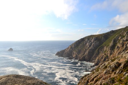 sea hitting seashore beside brown rock mountains under blue sky