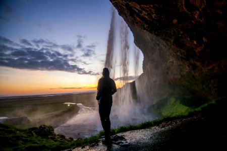 person standing under cave near waterfall photo