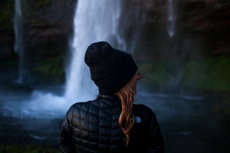 photo of woman wearing black jacket near waterfall photo