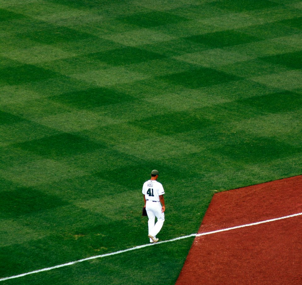 baseball player standing on field steps on white line at daytime