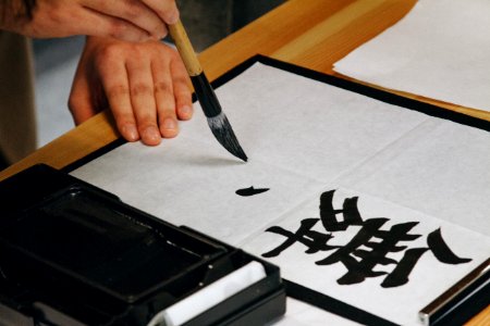 person holding black paint brush while painting black text on white paper photo