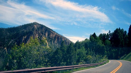 grey road surrounded by green trees overlooking mountain during daytime photo