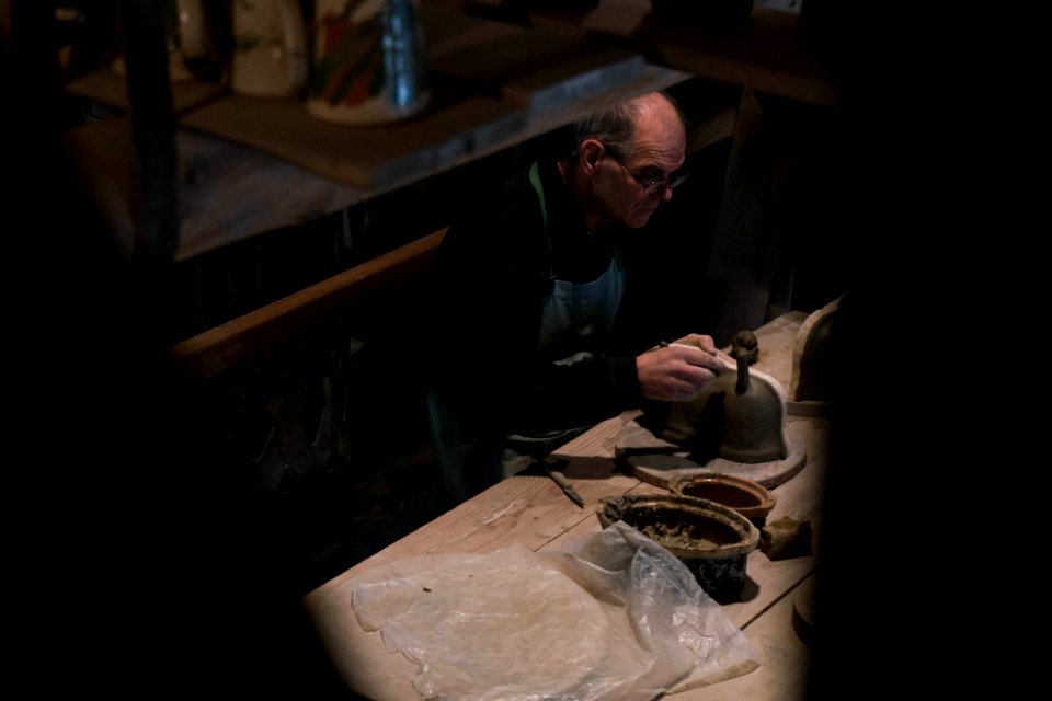 man in black long-sleeved shirt and blue apron working on gray pot on table