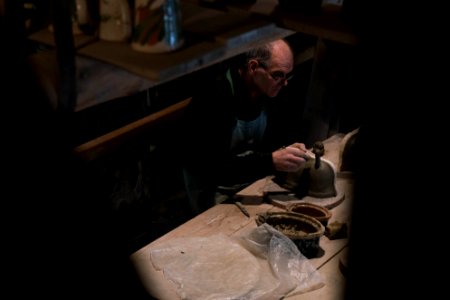 man in black long-sleeved shirt and blue apron working on gray pot on table