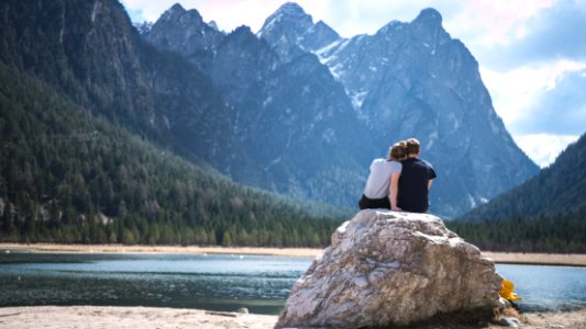 a couple sits on a rock looking out over a lake photo