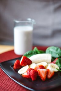 sliced strawberries and bananas on black plate beside white liquid-filled clear drinking glass photo
