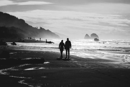 grayscale photo of man and woman walking on seashore photo