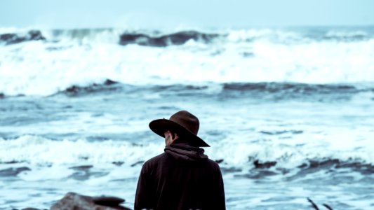 man wearing brown hat standing in front of ocean photo