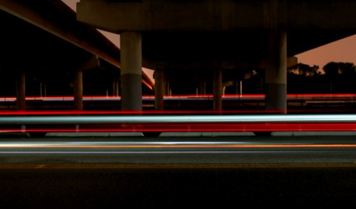 timelapse photography of vehicle light crossing on road under concrete dock