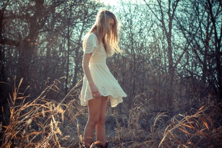 woman wearing dress standing on plant field near bare trees photo