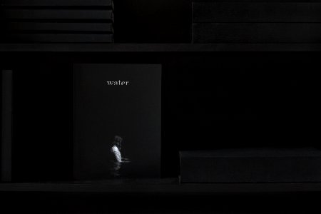 Shelf with books that is dark except for "water" magazine with a person wading on cover