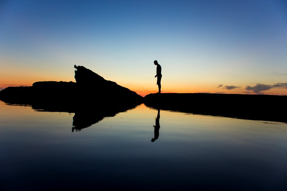 silhouette of man standing on land near body of water with reflection