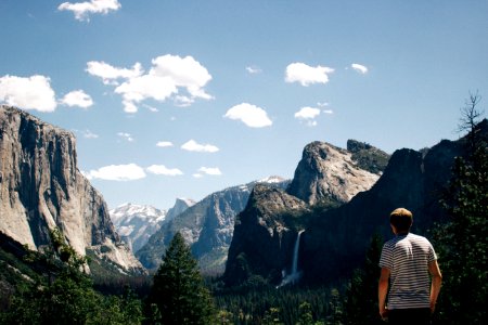man standing next to mountains with waterfalls and trees