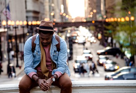 A man in a leather jacket looking down while sitting on a ledge in a city photo