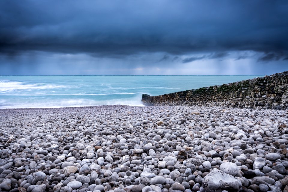 body of water across pebbles under dark sky