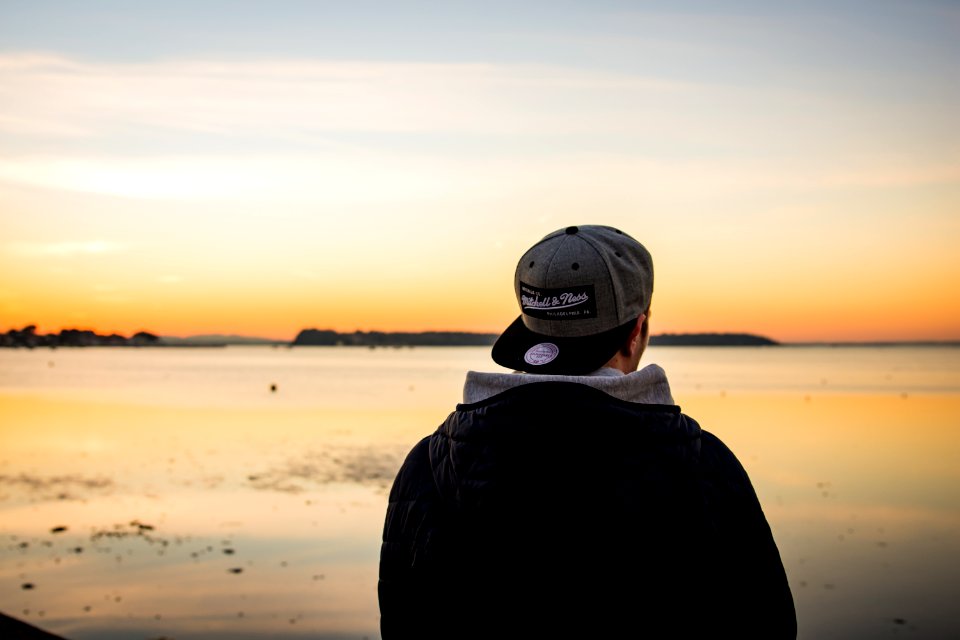 man wearing cap standing facing body of water