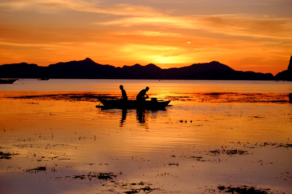 silhouette of two people riding boat on body of water during golden hour