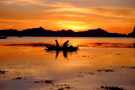 silhouette of two people riding boat on body of water during golden hour