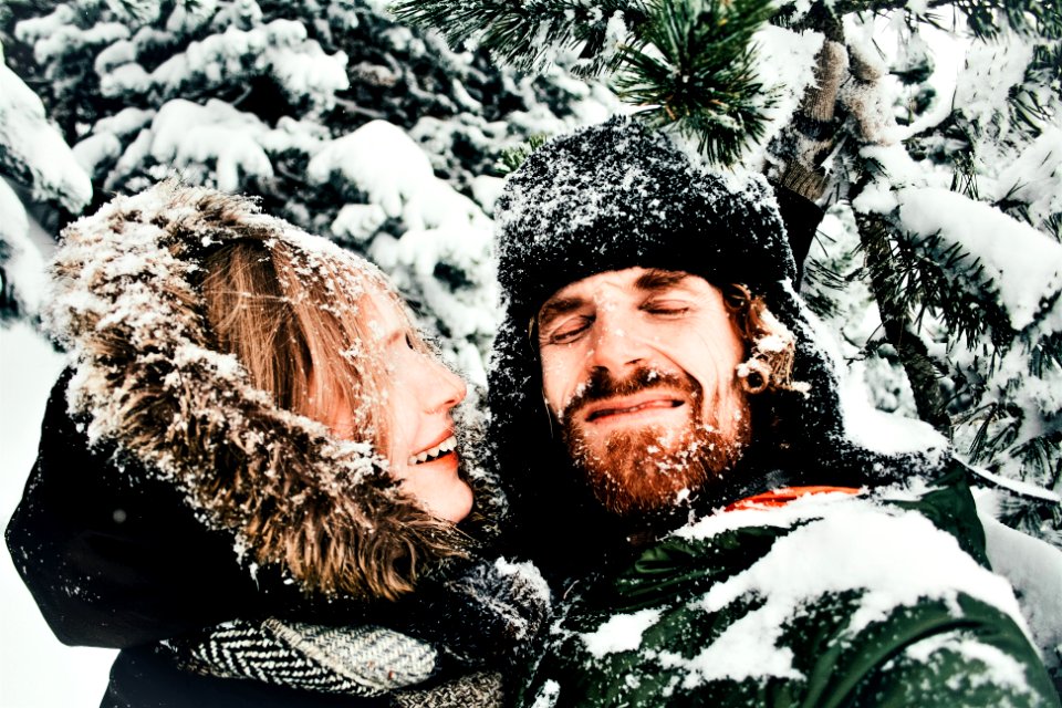 smiling man and woman standing under snow covered tree