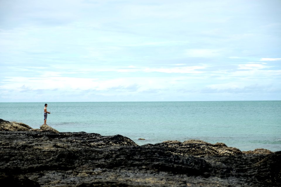 man standing on cliff fronting calm body of water