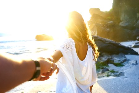 person holding woman's hand beside sea while facing sunlight photo