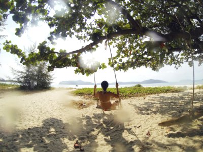 woman sitting on swing under green tree facing body of water at daytime photo
