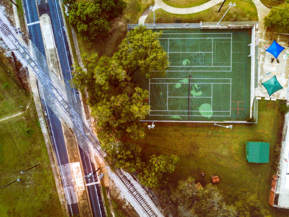 high angle photo of green lawn tennis court near trees, road, and railway