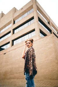 woman with hand on hair standing in front of brown wall photo