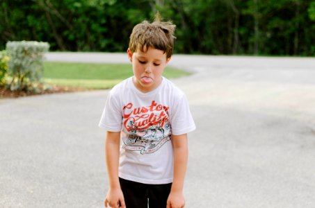 boy standing on gray concrete road while tongue out photo