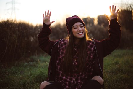 A happy woman sitting outside smiling with her hands raised to the sky.