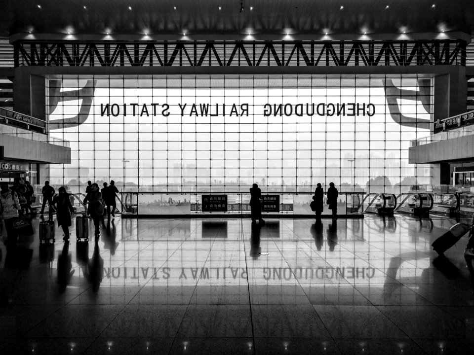 Black and white shot of station foyer with people and large window and reflection on floor