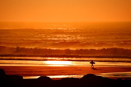 person holding surfboard walking on seashore during golden hour photo