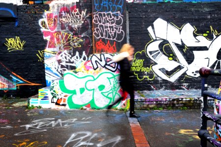 panning photography of woman walking beside wall with graffiti art