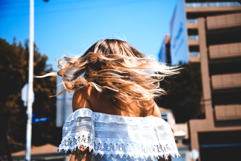 photo of woman wearing white off-shoulder crop top standing beside concrete building under clear blue sky