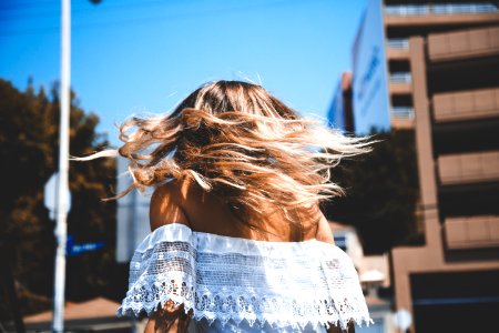 photo of woman wearing white off-shoulder crop top standing beside concrete building under clear blue sky photo