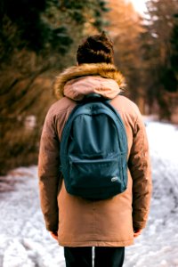 back photo of woman wearing brown parka hoodie and green backpack on snow photo