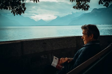 man sitting while holding a book watching on body of water photo