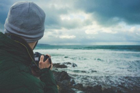 man holding DSLR camera taking picture of beach waves photo
