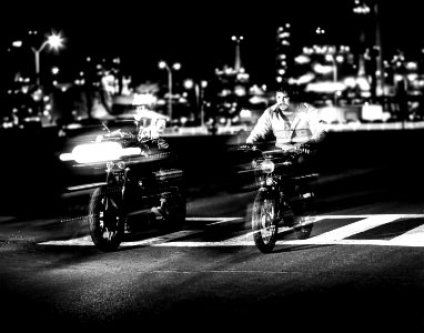 grayscale photo of person riding motorcycle near building and street lights