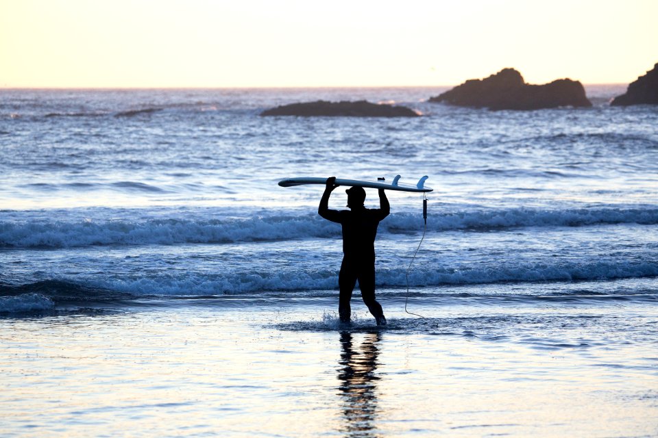 silhouette of man holding surfing board in seashore during daytime