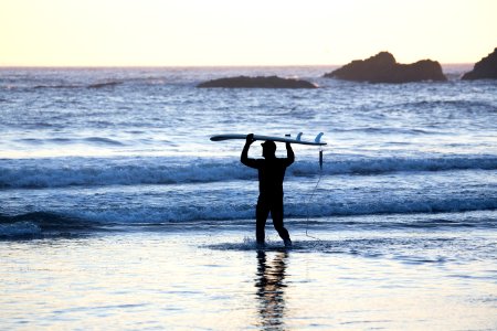 silhouette of man holding surfing board in seashore during daytime photo
