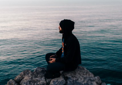 man sitting on rock near ocean water photo