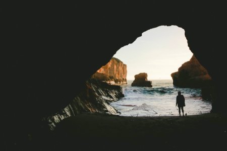 silhouette of person standing near body of water inside cave photo