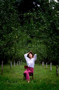 woman sitting on brown armless chair while tying her hair under green trees at daytime photo