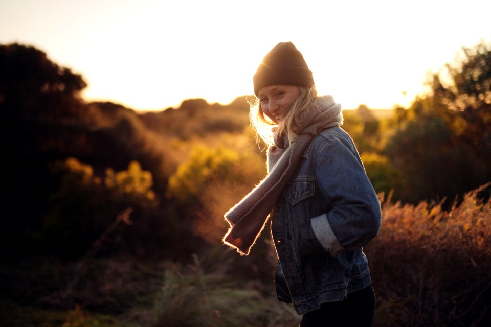 smiling woman taking photo near trees and brown grass during sunrise