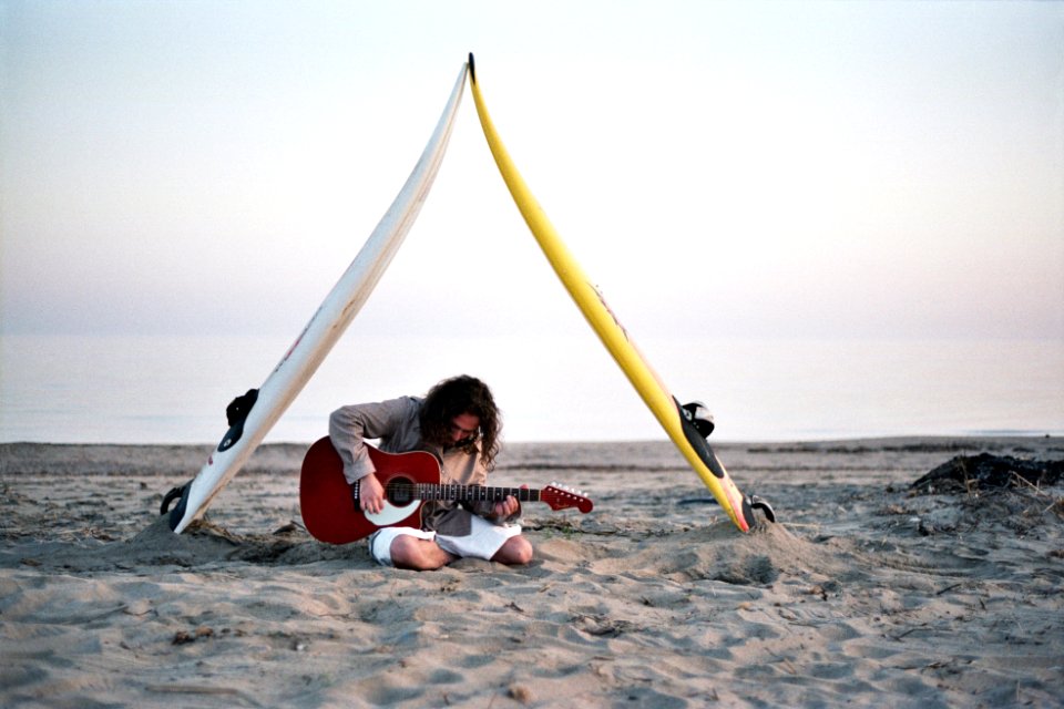 man playing guitar sitting on gray sand under cloudy sky