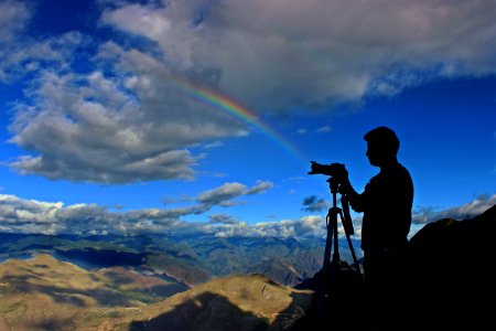 silhouette photo of holding camera with stand during daytime with rainbow photo