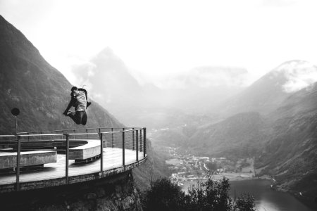 grayscale photo of man jumping near mountains photo